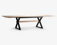 Et langt, rektangulært bord med en lys træbordplade og sorte metalben i X-form. Bordet har et minimalistisk design med rene linjer og en solid konstruktion. Der er en matchende lys træbjælke, der løber vandret mellem benene for ekstra stabilitet.