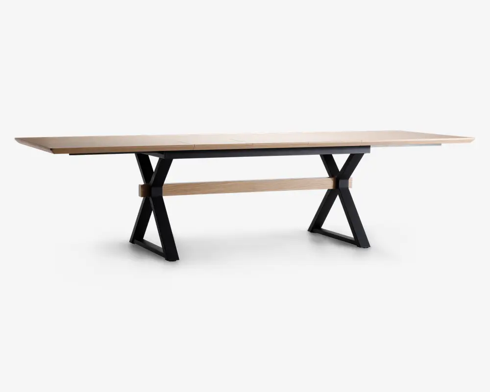 Et langt, rektangulært bord med en lys træbordplade og sorte metalben i X-form. Bordet har et minimalistisk design med rene linjer og en solid konstruktion. Der er en matchende lys træbjælke, der løber vandret mellem benene for ekstra stabilitet.