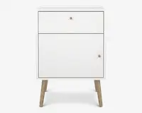 Et kompakt, moderne natbord med en ren hvid finish. Det har en enkelt skuffe øverst med en lille rund metalknop og en større skabsdør nedenunder, også med en matchende knop. Natbordet står på fire skråtstillede ben i lyst træ, hvilket giver det et udtryk i midcentury-stil. Designet er minimalistisk og funktionelt, velegnet til forskellige soveværelsesindretninger.
