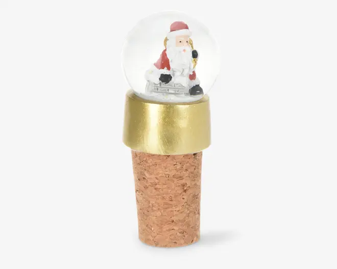 Flaskestopper af kork med en dekorativ snekugle på toppen, der indeholder en lille julemandsfigur indeni. Snekuglen er monteret i en guldfarvet base, hvilket giver et festligt udtryk. Korkdelen er naturlig og struktureret, designet til at passe sikkert i flaskehalsen.