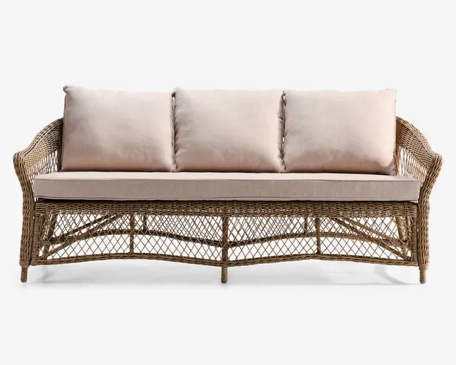 Tremandssofa med stel af naturligt flettet rattan og lyse beige hynder. Ryglænet har tre store, bløde puder for støtte, mens sædet har én tyk hynde for komfort. Armlæn og bund har et åbent, krydset fletmønster, som giver et let og afslappet udtryk. Benene er korte og integreret i stellet for stabilitet.