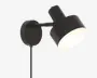 En moderne vægmonteret lampe med mat sort finish. Lampen har en cylindrisk skærm, der kan justeres for at rette lyset, og er fastgjort til en rund vægplade med en kort arm. Designet er minimalistisk og funktionelt, velegnet til læsning eller stemningsbelysning. Lampen har en synlig ledning, der går ned fra basen.