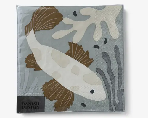 Kvadratisk serviet med en stiliseret illustration af en fisk med hvid krop og lysebrune finner, der svømmer blandt abstrakte tangformer i beige, grå og brune nuancer. Baggrunden er støvet blågrå, og nederst til venstre er der et lille mærke med teksten 'DANISH DESIGN.' Servietten har en let prikket, tekstureret overflade.