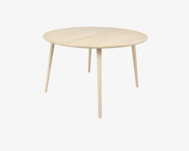 Et rundt bord med en lys træfinish, der har en glat, flad bordplade og fire slanke, let tilspidsede ben. Designet er minimalistisk og moderne med rene linjer og synlig træstruktur på overfladen.