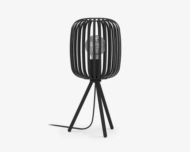 Moderne bordlampe med sort metalskærm i et bur-design, hvor lodrette stænger omkranser en synlig pære. Lampen står på tre skråtstillede ben og har en sort ledning, der går ud fra bunden. Designet er minimalistisk og industrielt, og pæren er i centrum af udtrykket.