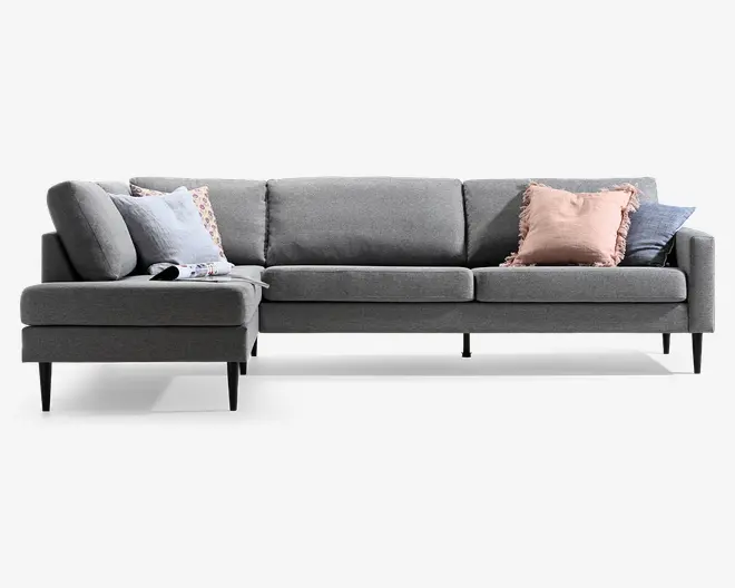Grå modulsofa med chaiselong til venstre, lave ryghynder, slanke sorte ben og flere pyntepuder i lyseblå, rosa og mørkegrå.