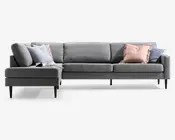 Grå modulsofa med chaiselong til venstre, lave ryghynder, slanke sorte ben og flere pyntepuder i lyseblå, rosa og mørkegrå.