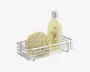 Rektangulær trådkurv med blank kromfinish, der indeholder en rund natursvamp og en høj, gennemsigtig flaske med sølvlåg og botanisk etiket. Kurven har et åbent gitterdesign, som giver dræning og synlighed af indholdet.