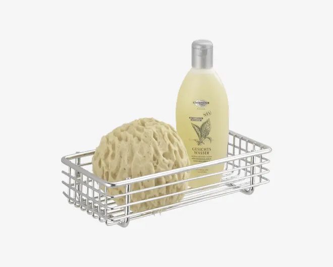 Rektangulær trådkurv med blank kromfinish, der indeholder en rund natursvamp og en høj, gennemsigtig flaske med sølvlåg og botanisk etiket. Kurven har et åbent gitterdesign, som giver dræning og synlighed af indholdet.