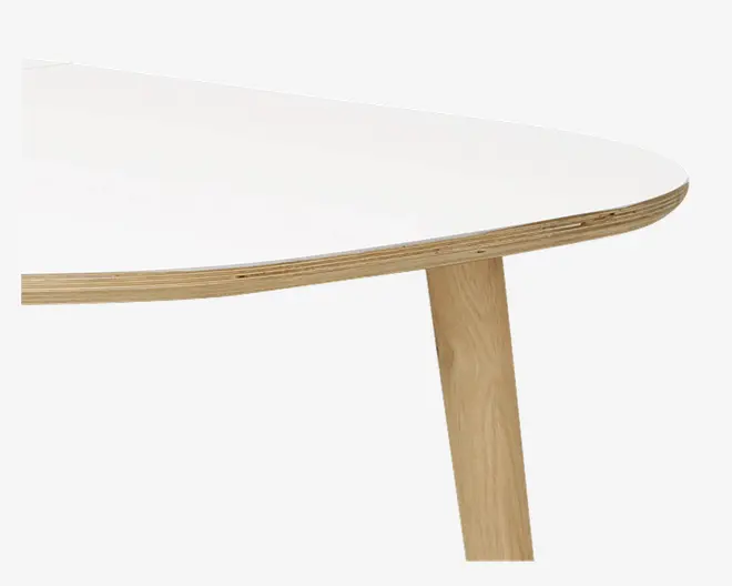 Nærbillede af et bordhjørne med en glat, afrundet hvid bordplade og synlig lagdelt trækant. Bordet har skråtstillede ben i lyst træ, hvilket giver et moderne og minimalistisk udtryk.