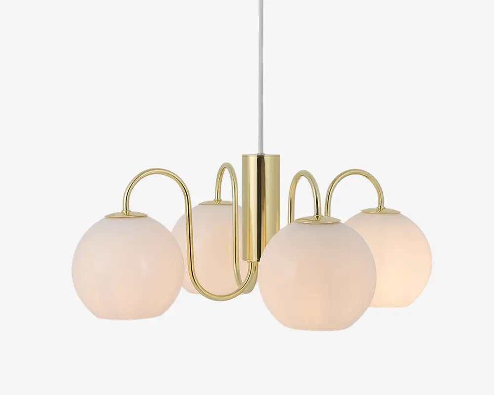 En moderne lysekrone med fire matte glasglobus-skærme, der er symmetrisk placeret omkring en central stang i guldfarvet metal. Hver globus holdes af en buet guldfarvet arm, hvilket giver et elegant og nutidigt udtryk. Lampen hænger i en hvid ledning, og det samlede design kombinerer et stilrent metaludtryk med blødt, diffust lys fra glasskærmene.