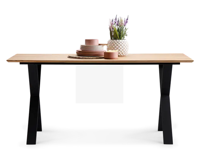 Rektangulært bord med en lys træbordplade og sorte, skråtstillede metalben. Bordpladen er pyntet med en stak lyserøde keramiktallerkener og skåle, en matchende kop, en rund fletbrik, en lille lyserød skål og en hvid vase med tekstur, der indeholder lilla og grønne kunstige blomster.