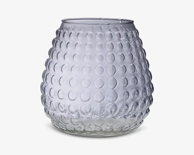 Klar glasbeholder med rund, bulet form og en tekstureret overflade med hævede cirkulære knopper arrangeret i et regelmæssigt mønster. Åbningen i toppen er lidt smallere end den bredeste del af kroppen. Glasset er gennemsigtigt og har et moderne, dekorativt udseende.