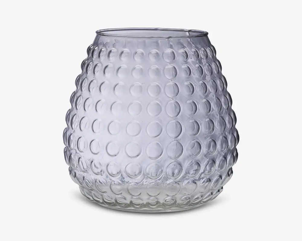 Klar glasbeholder med rund, bulet form og en tekstureret overflade med hævede cirkulære knopper arrangeret i et regelmæssigt mønster. Åbningen i toppen er lidt smallere end den bredeste del af kroppen. Glasset er gennemsigtigt og har et moderne, dekorativt udseende.