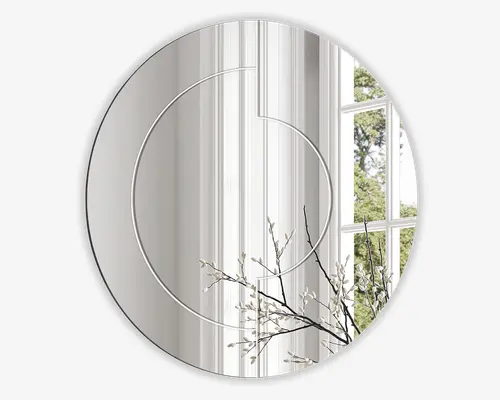 Rundt vægspejl med et moderne, minimalistisk design, der har to tynde, krydsende cirkellinjer indgraveret på overfladen. Spejlet har en klar refleksion og vises med en dekorativ gren med hvide knopper foran, hvilket tilføjer et elegant præg. Baggrunden inkluderer et lyst vindue og en hvid væg, hvilket fremhæver spejlets moderne stil.