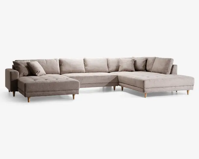 Rummelig L-formet sofa med chaiselong på venstre side, polstret i lysebeige stof. Har knapdetaljer på sædehynderne, bløde ryghynder og matchende pyntepuder for ekstra komfort. Sofaen står på korte, koniske træben, hvilket giver et moderne og solidt udtryk.