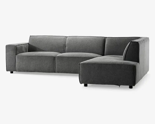 Moderne hjørnesofa med højrevendt chaiselong, betrukket med mørkegråt stof. Sofaen har brede, firkantede armlæn og dybe, bløde sædehynder for ekstra komfort. Ryglænet er lige og jævnt polstret, hvilket giver støtte langs hele sofaen. Den står på korte, solide ben, hvilket giver et lavt og stilrent udtryk. Sofaens rene linjer og minimalistiske design passer godt til moderne indretning.