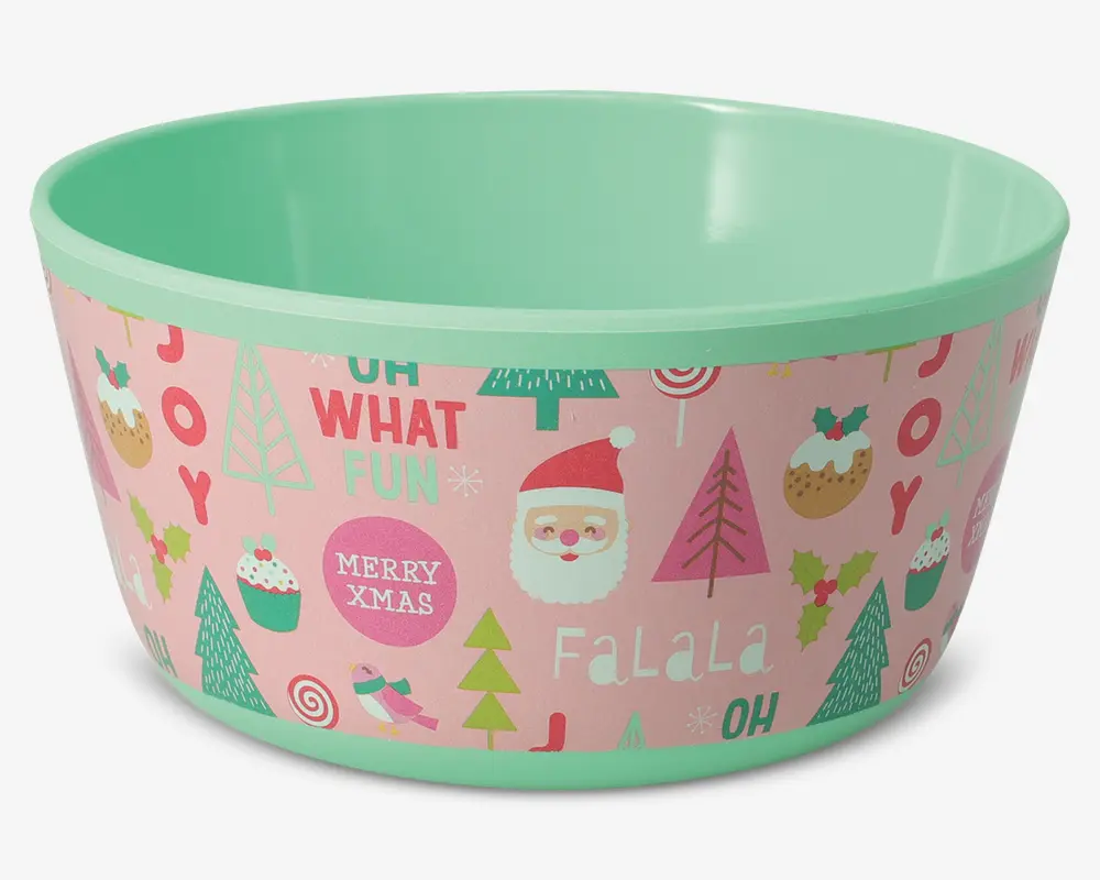 Rund skål med mintgrøn inderside og kant, og en yderside med festligt design på lyserød baggrund. Skålens yderside er dekoreret med julemotiver som julemand, juletræer, cupcakes, småkager, fugle og slik, samt ord som 'JOY', 'OH WHAT FUN', 'MERRY XMAS' og 'FALALA' i forskellige farver og skrifttyper.