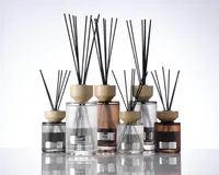 En samling dekorative glasbeholdere med lodrette rillede strukturer, hver med et lyst trælåg og fyldt med sorte duftpinde. Beholderne varierer i størrelse og farve, herunder klare, røggrå og ravfarvede nuancer. Hver beholder har en metallabel på forsiden, hvilket giver et eksklusivt og elegant udtryk. Det samlede design er moderne og stilfuldt, velegnet til boligindretning.