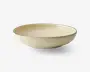 En rund, lav skål med en glat, blank cremefarvet overflade. Skålens kant er markeret med en tynd, mørk streg, som giver et diskret og elegant udtryk. Skålen har blødt skrånende sider og en flad bund, velegnet til servering af salater, pasta eller andre retter.