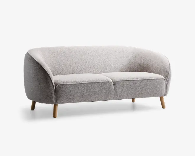 Et moderne, lysegråt polstret siddemøbel med buet ryglæn og armlæn, der flyder sammen med den samlede form. Sædet består af to bløde puder, og møblet står på fire let skrå, lyse træben, hvilket giver et stilrent og minimalistisk udtryk.