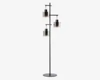 Høj gulvlampe med en rund, stabil base og en slank sort metalramme. Lampen har tre separate arme i forskellige højder, hver med en cylindrisk glasskærm med en farvegradient, der går fra mørk i toppen til klar i bunden. Lampen har et moderne, geometrisk design og giver lys i flere retninger.