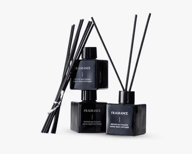 Sæt med tre elegante, sorte, firkantede glasflasker med matchende sorte låg, hver mærket med 'FRAGRANCE' og 'Pepper Balthazar Home Reed Diffuser.' Hver flaske indeholder flere lange, tynde sorte duftpinde til at sprede duften. Designet er moderne og minimalistisk med en blank finish, der giver et luksuriøst udtryk.