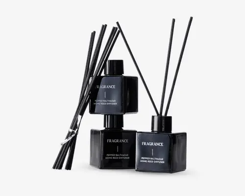 Sæt med tre elegante, sorte, firkantede glasflasker med matchende sorte låg, hver mærket med 'FRAGRANCE' og 'Pepper Balthazar Home Reed Diffuser.' Hver flaske indeholder flere lange, tynde sorte duftpinde til at sprede duften. Designet er moderne og minimalistisk med en blank finish, der giver et luksuriøst udtryk.