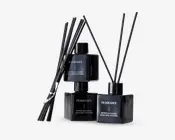 Sæt med tre elegante, sorte, firkantede glasflasker med matchende sorte låg, hver mærket med 'FRAGRANCE' og 'Pepper Balthazar Home Reed Diffuser.' Hver flaske indeholder flere lange, tynde sorte duftpinde til at sprede duften. Designet er moderne og minimalistisk med en blank finish, der giver et luksuriøst udtryk.