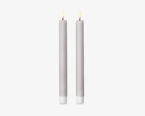 Sæt med to høje, slanke, cylindriske genstande med en glat, mat lysegrå overflade. Hver har en realistisk flammeformet spids i toppen, hvilket antyder, at de er designet til at ligne traditionelle stearinlys. Basen er flad og en smule bredere for at give stabilitet. Det samlede design er minimalistisk og moderne.