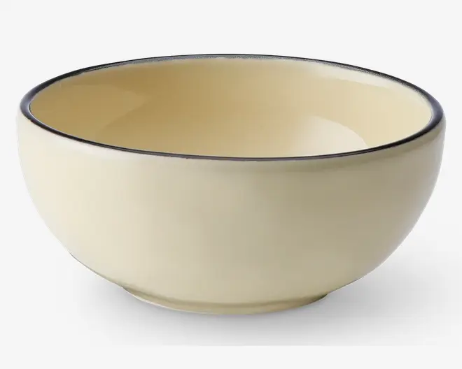 Rund skål med en glat, blank cremefarvet overflade både indvendigt og udvendigt. Skålens kant har en diskret mørk accentlinje, som giver et elegant kontrast til det enkle design. Skålen har en blødt buet form og en let forhøjet bund for stabilitet.