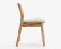 Sidebillede af en stol med stel i lyst træ, let buet ryglæn og ben. Sædet er polstret og betrukket med et lysebeige stof for ekstra komfort. Designet er minimalistisk og moderne med rene linjer og en naturlig træfinish.