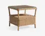 Firkantet sidebord fremstillet af naturfarvet flettet rattan med en glastop, der giver en jævn overflade. Bordet har en ekstra hylde nederst til opbevaring eller udstilling og står på fire solide, runde ben. Den flettede struktur giver et afslappet og let udtryk, der passer til både indendørs og udendørs brug.