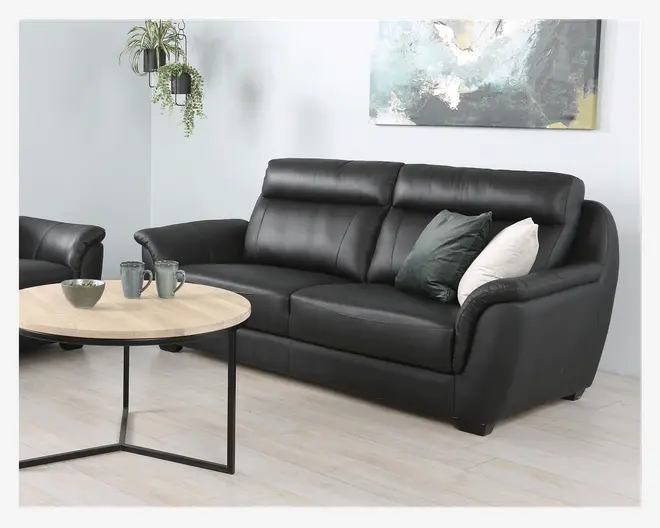 En moderne sort lædersofa med tre siddepladser, polstrede hynder og høje ryglæn for ekstra komfort. Armlænene er let buede, og sofaen har to pyntepuder – én mørkegrøn og én hvid. Sofaen står på korte, solide ben og har et stilrent, moderne design, der passer til stuen.