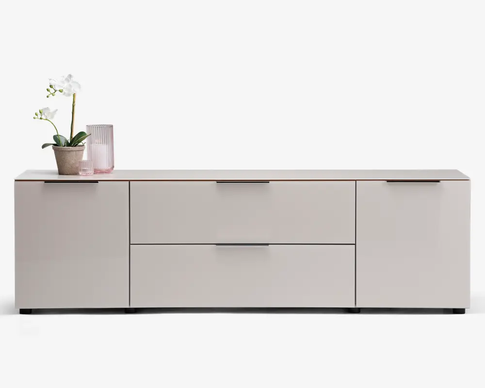 Et moderne, lavt opbevaringsmøbel med mat lysegrå finish. Det har to store centrale skuffer med slanke, vandrette greb, flankeret af to skabslåger på hver side, hver med matchende greb. Topfladen er flad og rummelig, velegnet til dekoration; på billedet står en potteorkidé og en rillet glasvase. Designet er minimalistisk med rene linjer og uden synlig udsmykning.