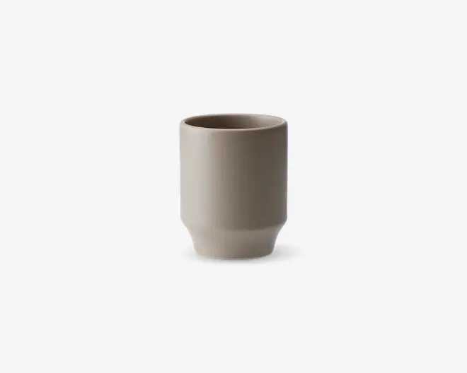 En minimalistisk, cylindrisk kop med en glat mat beige overflade. Koppen har lige sider og en let afrundet bund, hvilket giver den et moderne og enkelt udtryk. Der er ingen hank eller dekorative detaljer, hvilket understreger det rene og funktionelle design.