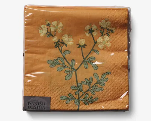 Kvadratisk serviet i papir med varm orange baggrund, dekoreret med en botanisk illustration af en grøn stilk med lysegule blomster og grønne blade. Servietten har en diskret prikket struktur langs kanterne og er pakket i klar plastik. Et lille mærkat i hjørnet viser teksten 'Danish Design.'