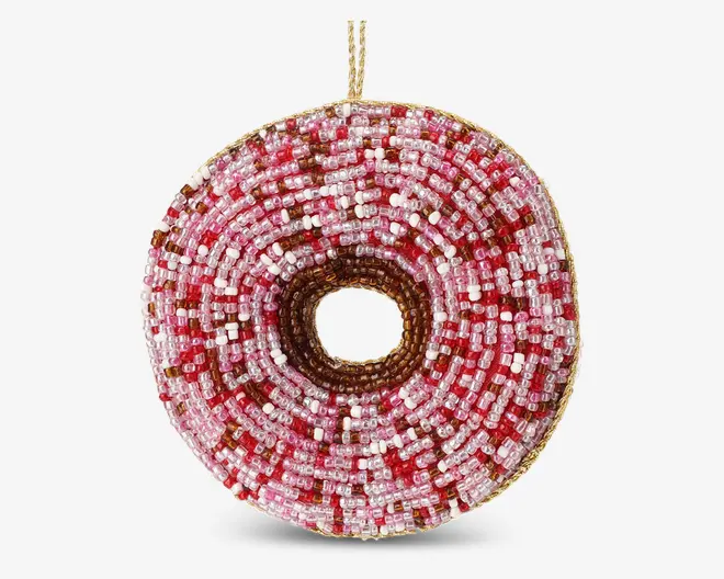 Rundt ornament designet til at ligne en donut, dækket med små glasperler i nuancer af pink, rød, hvid og brun. Perlerne er arrangeret i koncentriske cirkler, hvilket giver en tekstureret og farverig overflade. Ornamentet har en lille gylden ophængsløkke øverst.