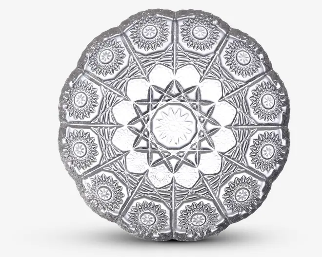 Rund, klar glasplade med indviklede geometriske og blomstrede mønstre præget på overfladen. Designet har et centralt stjernemotiv omgivet af trekantede sektioner, der hver indeholder en mindre blomsterroset. Tallerkenen har en bølget kant, hvilket giver et dekorativt udtryk.