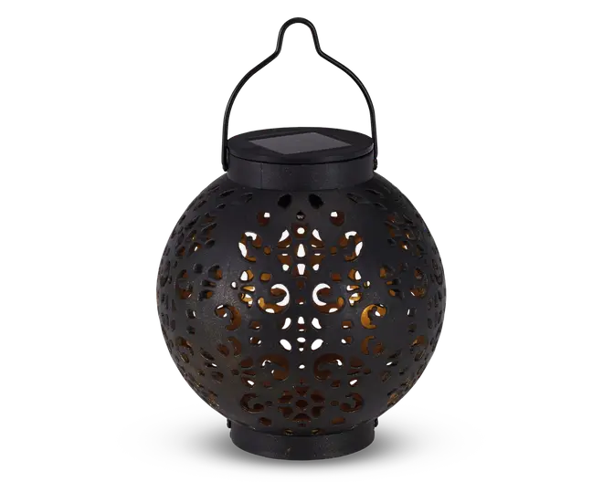 Rund sort lanterne med indviklede udskæringer i overfladen, som lader et varmt gult lys skinne igennem. Lanternen har et håndtag øverst til ophængning og et solcellepanel integreret i låget til opladning. Designet skaber dekorative lysmønstre, når den er tændt.