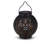 Rund sort lanterne med indviklede udskæringer i overfladen, som lader et varmt gult lys skinne igennem. Lanternen har et håndtag øverst til ophængning og et solcellepanel integreret i låget til opladning. Designet skaber dekorative lysmønstre, når den er tændt.