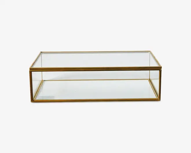 Rektangulær glasmontre med guldfarvet metalramme. Boksen har klare glasplader på alle sider, inklusive top og bund, og har rene, lige kanter. Den gyldne ramme giver et elegant og sofistikeret udtryk, hvilket gør den velegnet til at udstille smykker, samlerobjekter eller dekorative genstande.