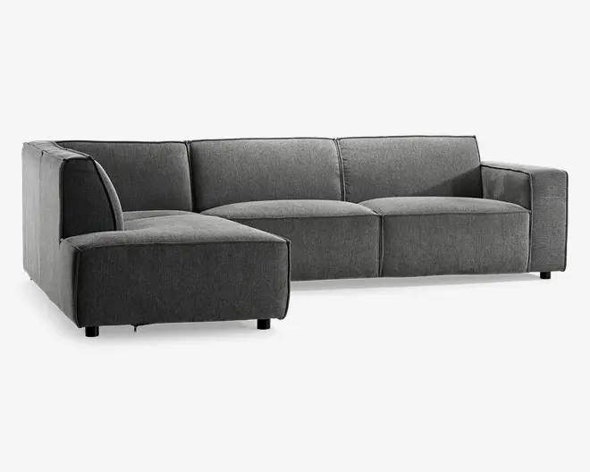 Moderne hjørnesofa med venstrevendt chaiselong, betrukket med mørkegråt stof. Sofaen har brede, flade armlæn og dybe, bløde sædehynder for ekstra komfort. Ryghynderne er faste og jævnt placeret, hvilket giver god støtte. Sofaen står på korte, solide ben, hvilket giver et lavt og stilrent udtryk. De rene linjer og minimalistiske design passer godt til moderne indretning.