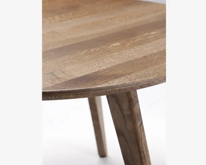 Nærbillede af en rund bordplade i træ med naturlig træstruktur. Bordpladens kant er let affaset, og overfladen viser forskellige trænuancer og synlig tekstur. Et solidt, skråtstillet træben ses, som matcher bordpladens farve og åretegning.