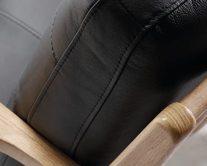 Nærbillede af en sort læder sopude med synlige syninger, fastgj Sally til en lys træramme. Læder pipeline har en let resurface, og syningerne fremstår pæne og outside. Trærammen har en glat, poleret overflade, der fremhæver træets naturlige årer.