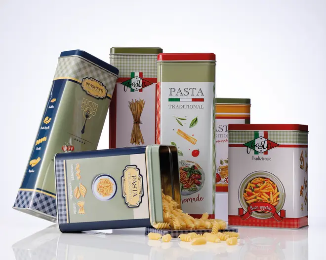 En gruppe dekorative, rektangulære metaldåser i creme, rød, blå og grøn med italiensk inspirerede etiketter, ternede detaljer og illustrationer af pasta. Én dåse ligger på siden, mens tør pasta vælter ud på overfladen.