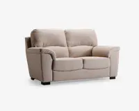 En to-personers sofa betrukket med lysebeige stof, med bløde, fyldige ryghynder og brede, polstrede armlæn. Sædehynderne er tykke og let afrundede for ekstra komfort. Sofaen står på korte, solide sorte ben, hvilket giver et moderne og hyggeligt udtryk.