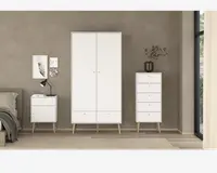 Billedet viser et sæt moderne soveværelsesmøbler i minimalistisk stil. Møblerne er hvide med lyse træben, der er let skråtstillede. Sættet består af et højt garderobeskab med to låger og to skuffer nederst, en kommode med fire skuffer og et natbord med én skuffe og en åben hylde. Håndtagene er små og runde, hvilket giver et rent udtryk. Overfladerne er glatte, og designet er enkelt, velegnet til moderne indretning.