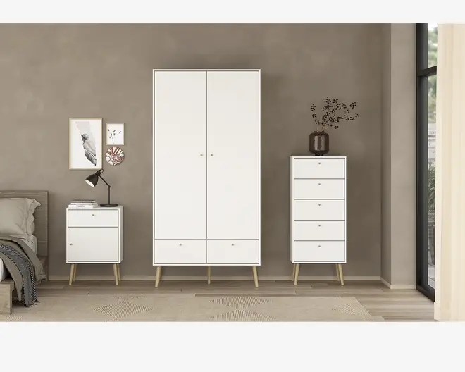 Billedet viser et sæt moderne soveværelsesmøbler i minimalistisk stil. Møblerne er hvide med lyse træben, der er let skråtstillede. Sættet består af et højt garderobeskab med to låger og to skuffer nederst, en kommode med fire skuffer og et natbord med én skuffe og en åben hylde. Håndtagene er små og runde, hvilket giver et rent udtryk. Overfladerne er glatte, og designet er enkelt, velegnet til moderne indretning.