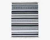 Rektangulært tekstil med vandrette striber i sort, hvid, grå og brune nuancer. Striberne varierer i bredde og har geometriske mønstre som prikker, diamanter og linjer. Kanterne er afsluttet med korte hvide frynser i begge ender.